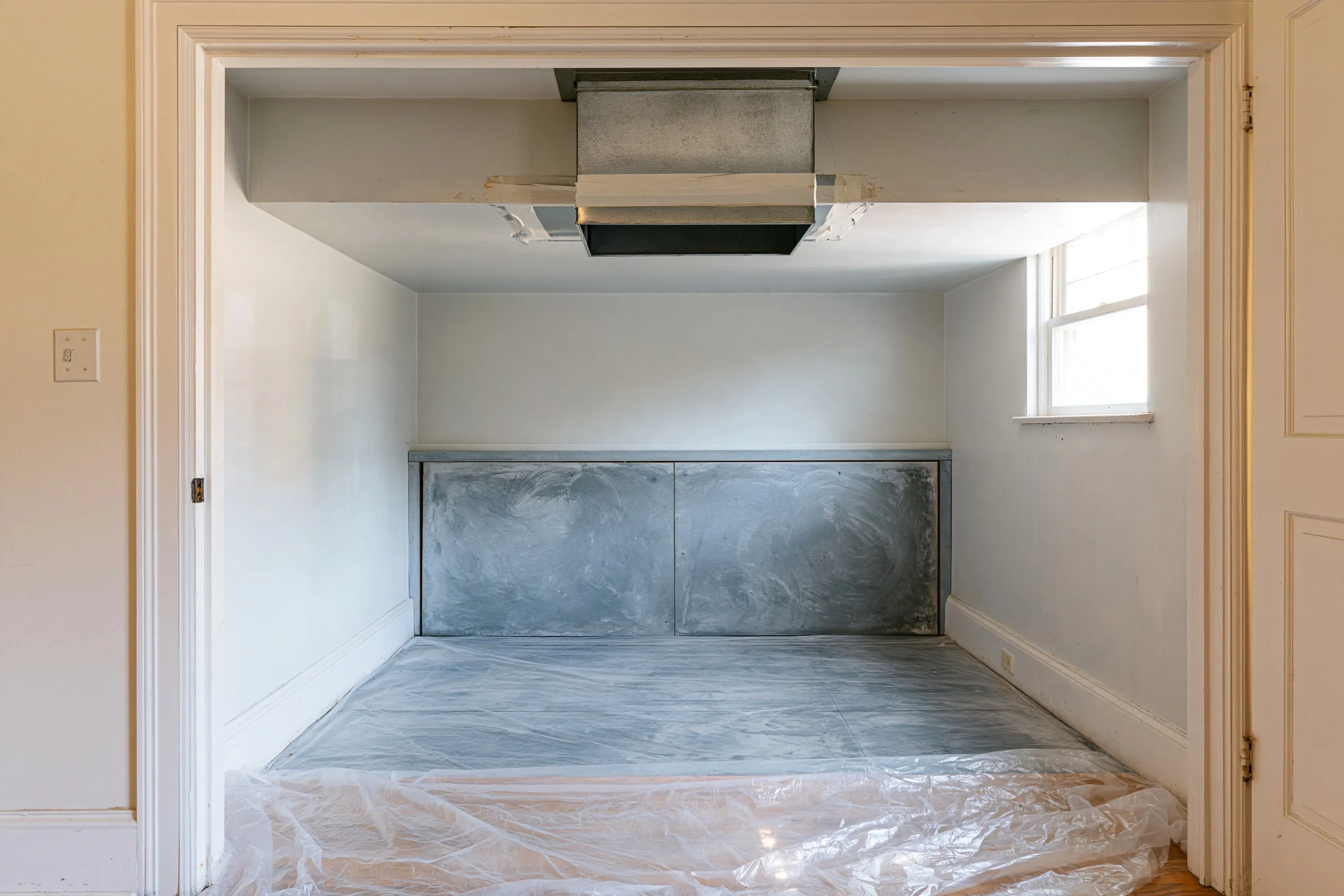 Hall HVAC closet with the old furnace removed, a sealed duct collar and a gray cement-board panel
